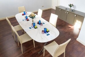 A dining area with a marble table, white chairs, and a cabinet with a plant.