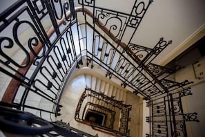 Una escalera de caracol con barandillas de metal ornamentadas y un muro de mármol.