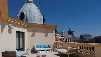 Una terraza en la azotea con sofá, sillón y mesa de centro, un edificio de forma abovedada al fondo y vistas de la ciudad.