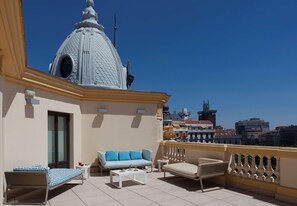 Une terrasse sur le toit, avec un canapé, un fauteuil et une table basse, un bâtiment en forme de dôme en arrière-plan et une vue sur la ville.
