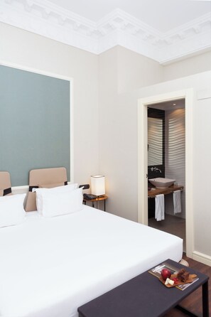 Ein Hotelzimmer mit einem großen Bett, einem Nachttisch mit Lampe, einem kleinen Tisch mit Snacks und einem durch eine offene Tür einsehbaren Badezimmer.