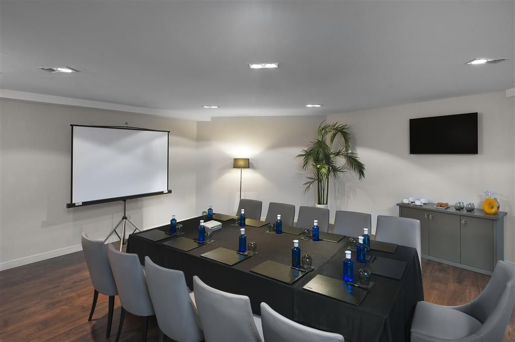 A conference room with a long table, chairs, a projector screen, a lamp, and a television on the wall.