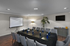 A conference room with a long table, chairs, a projector screen, a lamp, and a television on the wall. - Sardinero Madrid (Madrid)