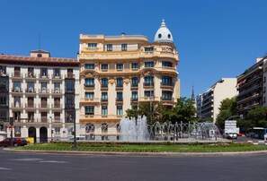 Ein Hotel mit einer klassischen Fassade, mehreren Balkonen und einer Springbrunnen vor der Tür.