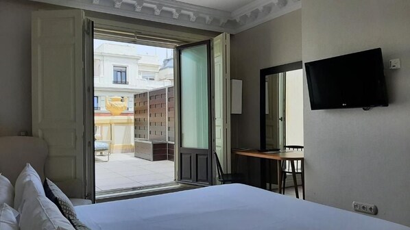 A hotel room with a bed, a desk, a television, and an open door leading to a balcony. - Sardinero Madrid (Madrid)