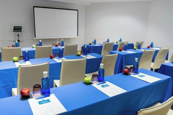 A conference room with multiple tables, each covered with a blue tablecloth, equipped with water bottles, apples, and name tags.