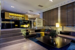 Un salon moderne avec un canapé, une table basse et un escalier menant à un espace bar appelé « The Library Lounge ».