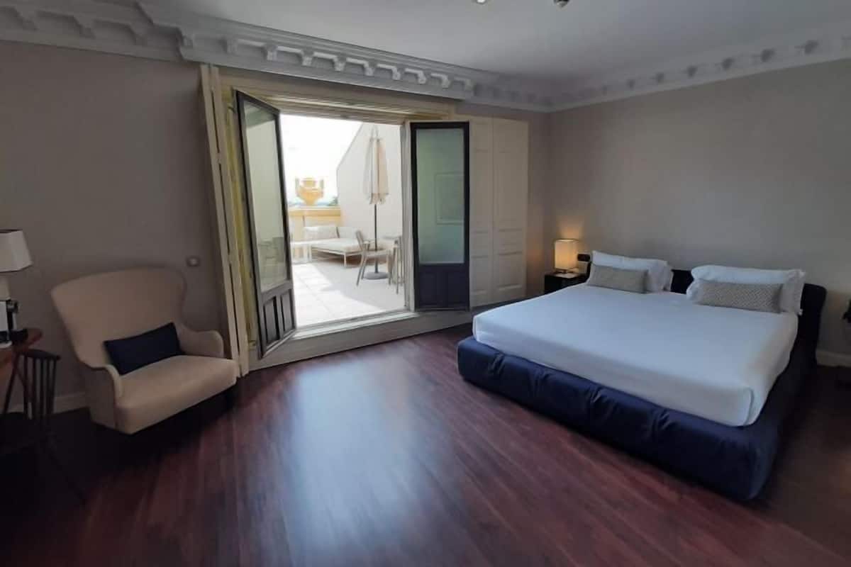 Une chambre d’hôtel avec un grand lit, une chaise, un bureau et une porte-fenêtre coulissante donnant sur un espace extérieur.