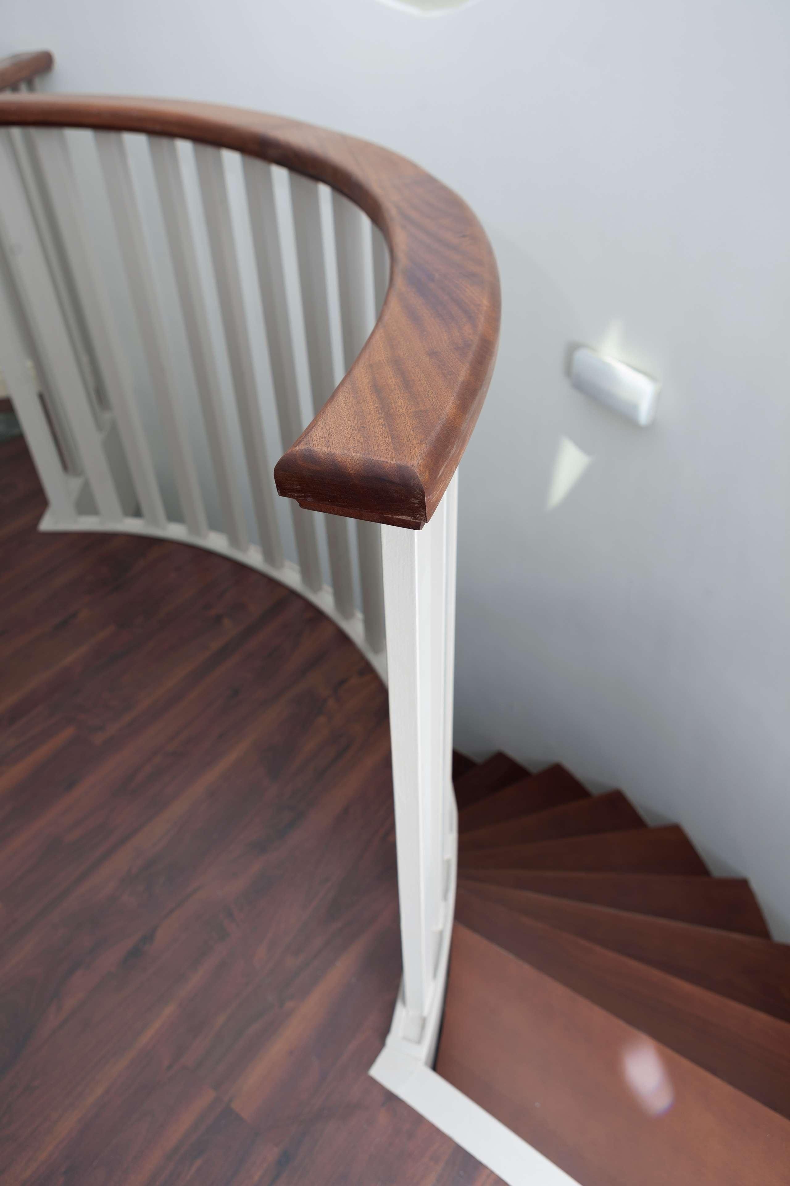 A wooden handrail with a white balustrade, a wooden staircase, and a white wall.