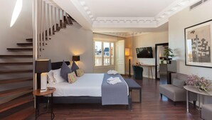 Een slaapkamer met een bed, nachtlampen, een bureau, een stoel, een bank, een televisie en een trap.