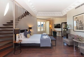 Ein Schlafzimmer mit Bett, Nachttischlampen, Schreibtisch, Stuhl, Sofa, Fernseher und einer Treppe.