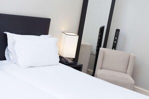 Ein Hotelzimmer mit Bett, Nachttisch mit Lampe, Stuhl und festmontiertem Telefon.