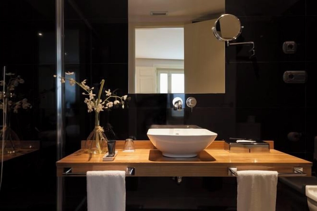 A modern bathroom with a large white sink, a mirror, and a vase with flowers on the counter.
