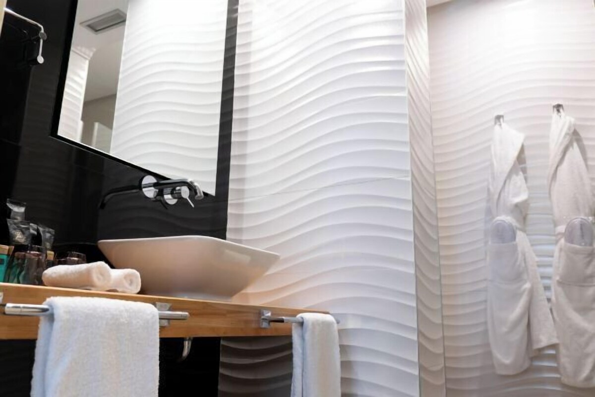 Une salle de bain avec un grand miroir, un lavabo et un porte-serviettes.