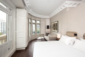 A hotel room with a large bed, a sofa, a small table, and a window with a view of buildings. - Sardinero Madrid (Madrid)
