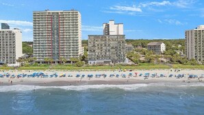 A beachfront hotel with multiple high-rise buildings, a sandy beach, and umbrellas.