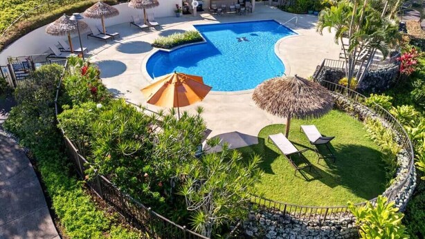 Una piscina rodeada de sillas de descanso, sombrillas y un pequeño edificio.