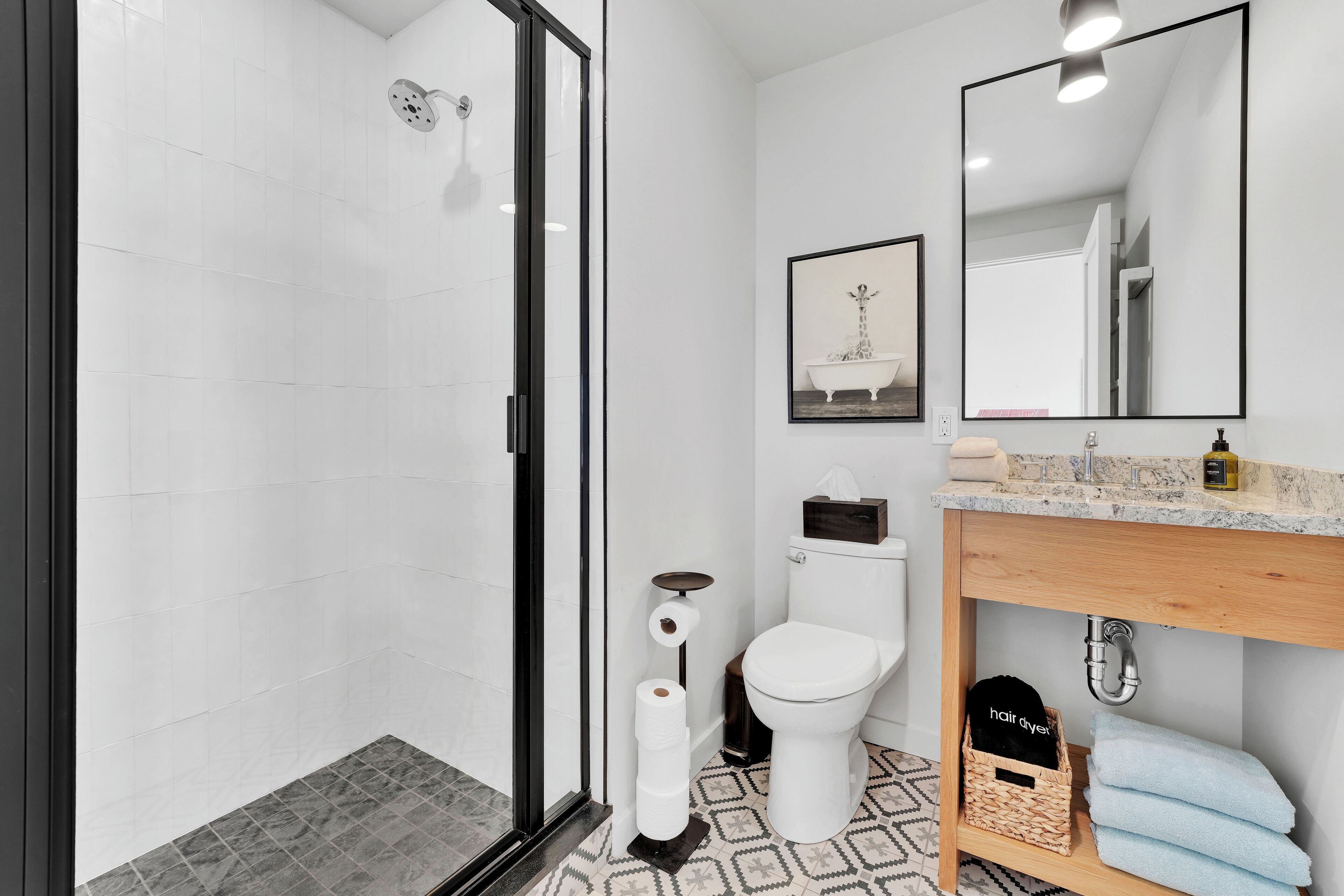 Un baño moderno con cabina de ducha de vidrio, un inodoro blanco, un lavamanos con encimera de madera y un espejo sobre el lavamanos.