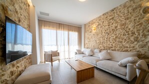 A modern living room with a stone wall, a flat-screen TV, a sofa, a chair, and a coffee table. - OSTALEA Boutique Rural House with Jacuzzi, near the beach and medieval villages. (Vilanova d'Alcolea)