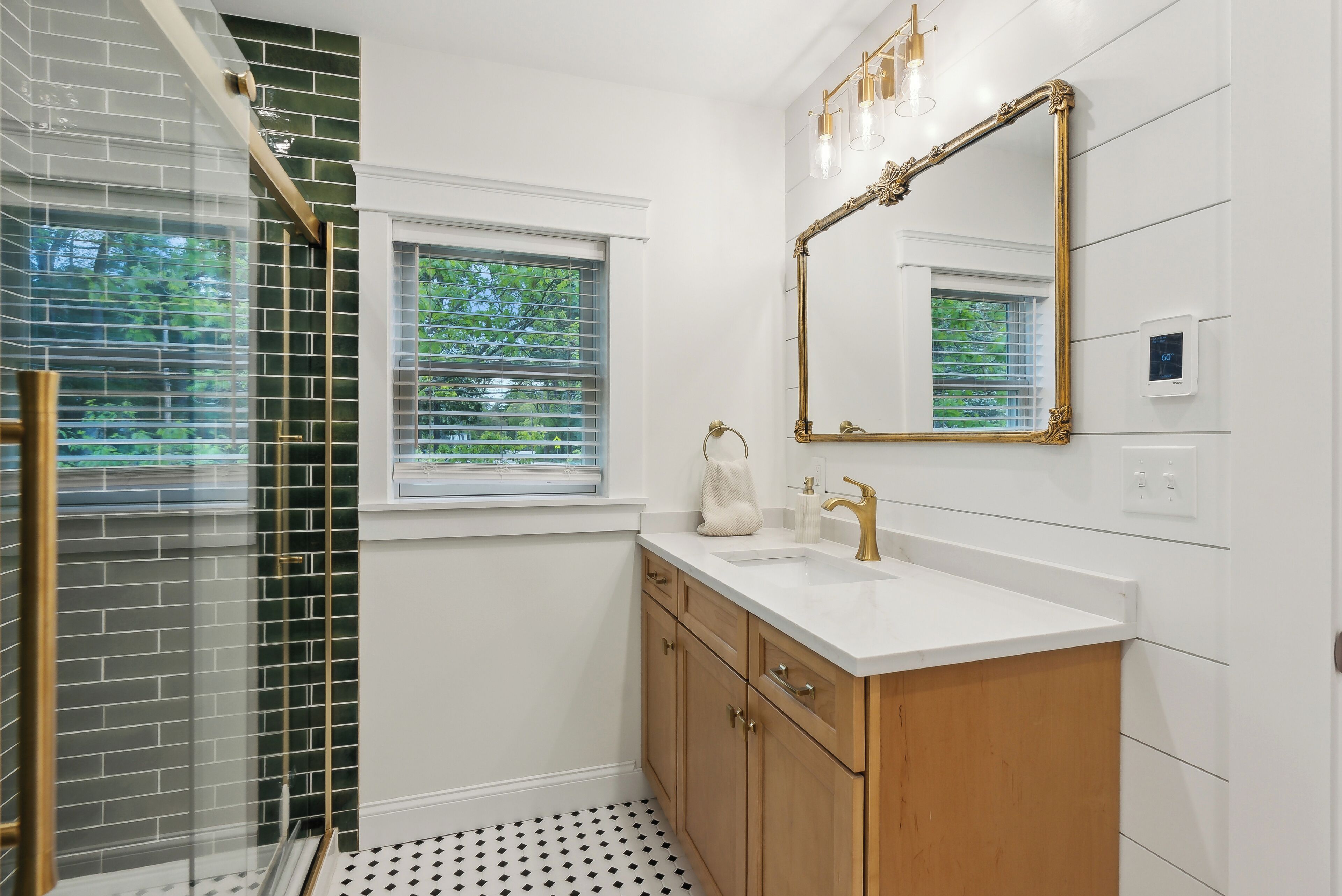 Une salle de bain avec un meuble-lavabo blanc, un miroir encadré d’or et une douche dotée d’une porte en verre.