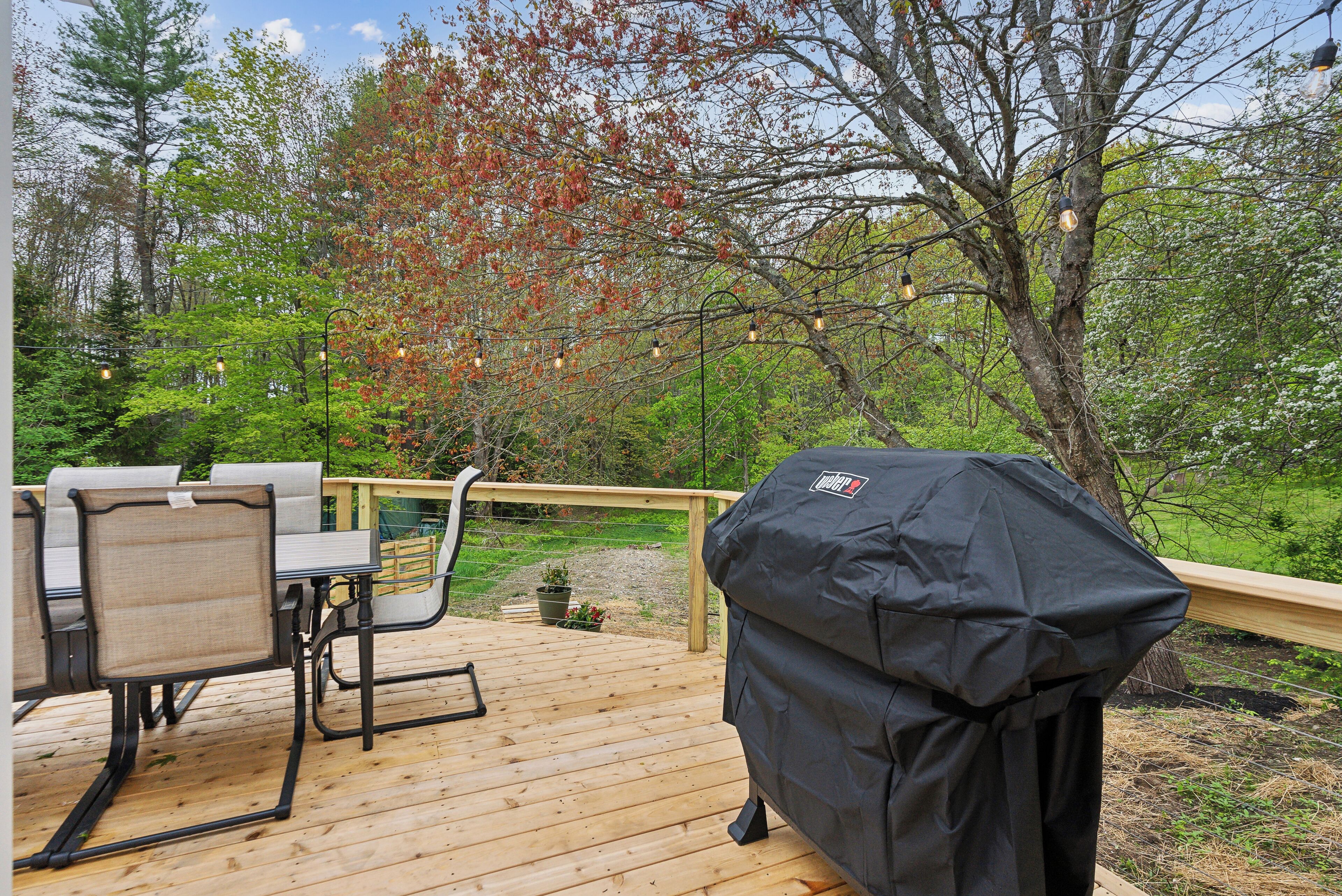 A wooden deck with outdoor furniture, a grill, and string lights.