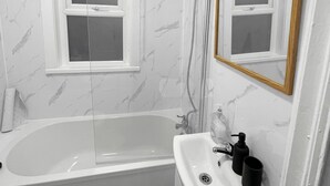 A bathroom with a bathtub, a sink, a mirror, and a window.