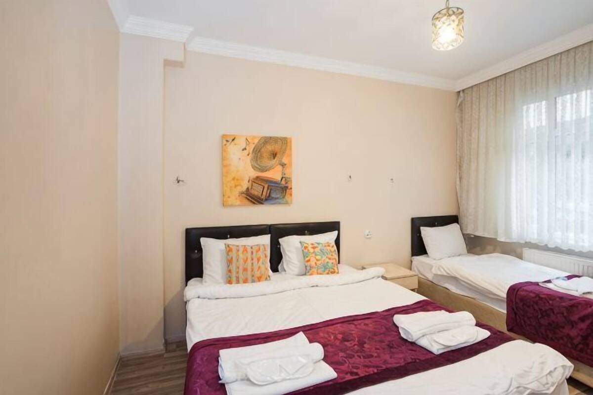 A hotel room with two beds, a painting on the wall, and a window with curtains.