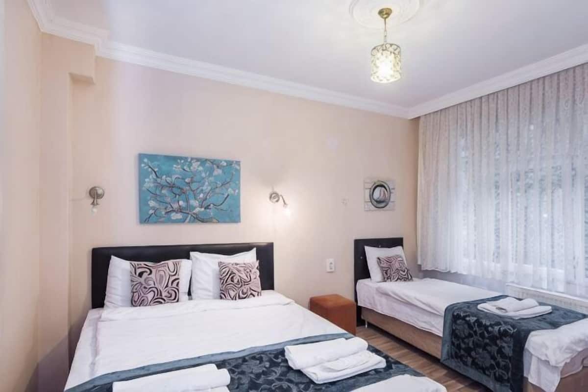 A bedroom with two beds, a painting, a chandelier, and a window with curtains.