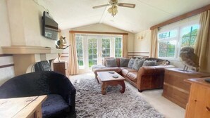 A cozy living room with a sofa, armchair, coffee table, and a television mounted on the wall. - Berney Lodge - Puppy Lounge, arcades, games room (Faldingworth)