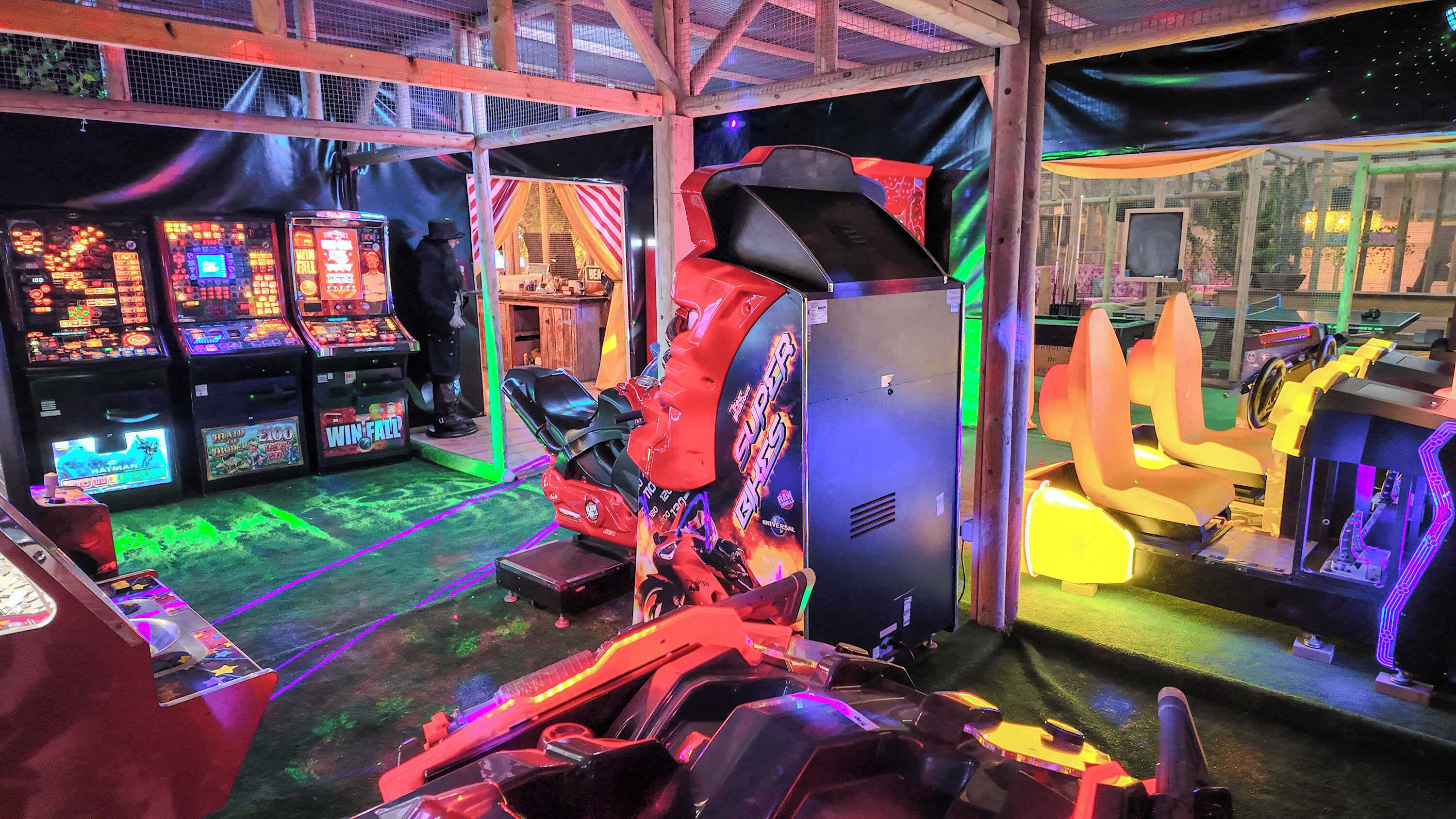 An indoor arcade with various gaming machines, a racing simulator, and a seating area.