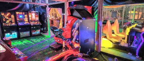 An indoor arcade with various gaming machines, a racing simulator, and a seating area.