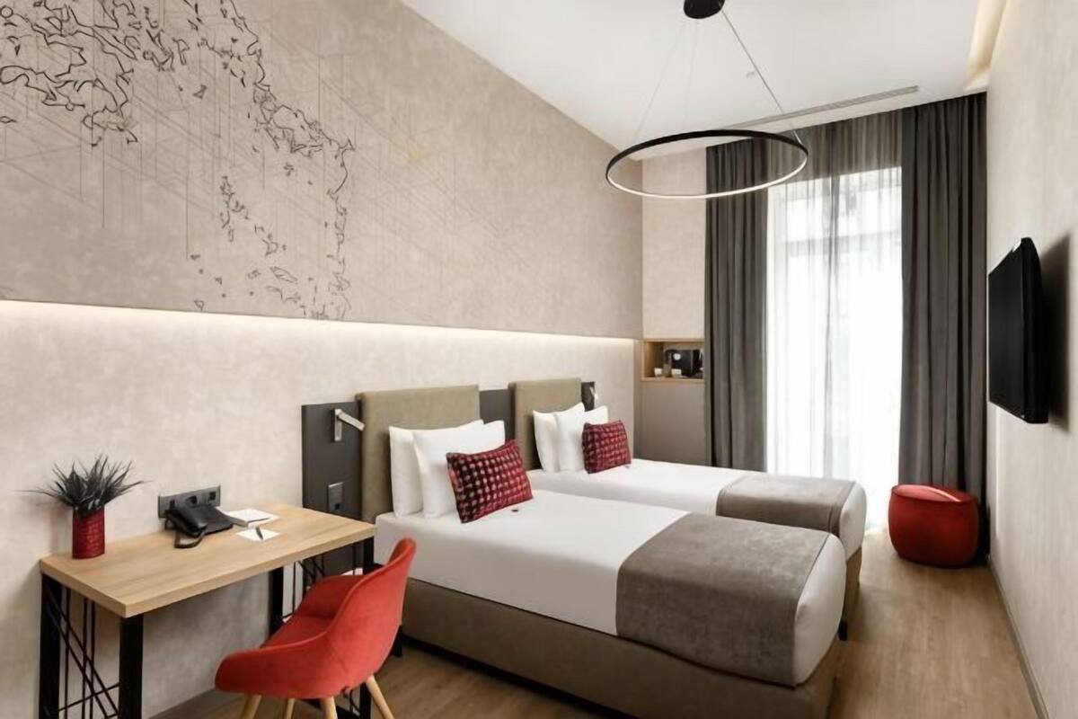 A modern hotel room with a large bed, a desk, a chair, a TV, and a map on the wall.