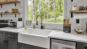 Een moderne keuken met een groot raam, witte aanrechtbladen en een inbouw vaatwasser.