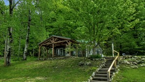 Een houten chalet met een veranda, omgeven door bomen en een stenen trap erheen.