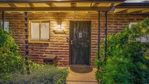 A rustic brick house with a dark wooden door, a small window, and a porch with a covered area. - Serene 3BR retreat with Catalina Mountain views, shaded gazebo, BBQ grill & dog-friendly backyard. (Tucson)