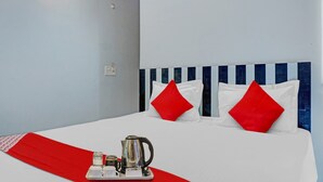 A hotel room with a bed, red pillows, a tray with a coffee pot, and a red runner. - Royal Comfort Homestay (Patna)