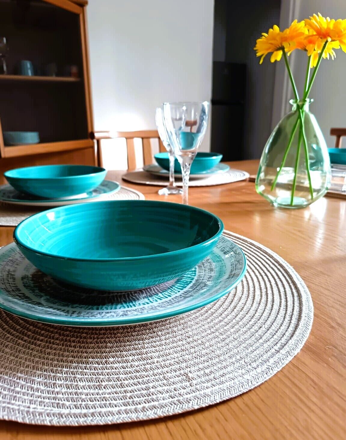 Ein Esstisch mit türkisfarbenen Schalen und einer klaren Glasvase mit gelben Blumen.