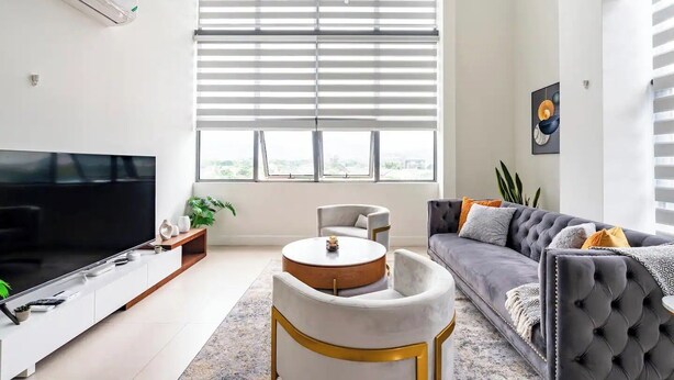 A modern living room with a flat-screen TV, a round coffee table, a grey sofa, and a large window with blinds. - Luxury Penthouse 3Bdr with pool (Kingston)