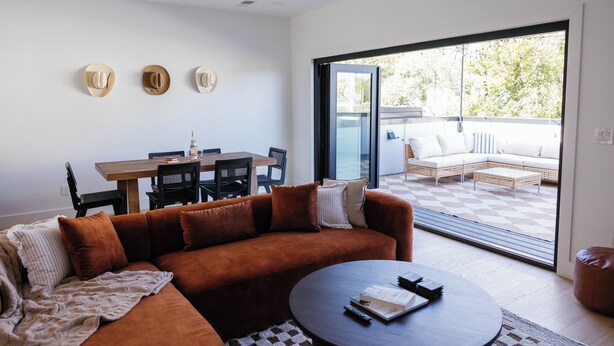 Ein modernes Wohnzimmer mit einem braunen Sofa, einem runden Couchtisch und einem Essbereich mit einem Holztisch und Stühlen.