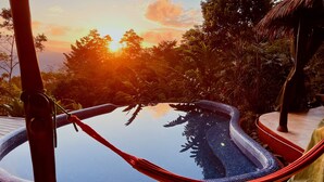 Una hamaca sobre una piscina con fondo de cristal y vista al atardecer.