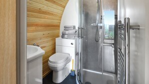 A modern bathroom with a wooden wall, a white toilet, a glass shower enclosure, and a stack of towels. - Luna Holiday Pod - UK48590 (Snailbeach)