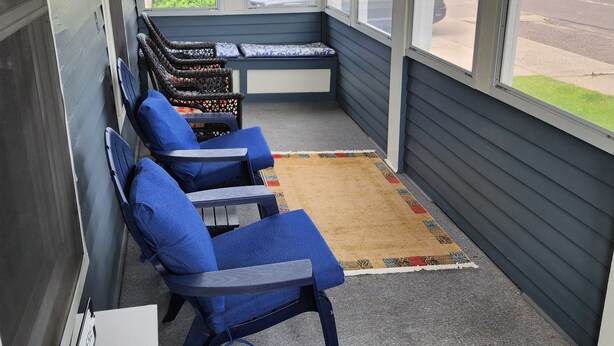 Een overdekt terras met blauwe stoelen en een bank, een klein tafeltje en een vloerkleed.