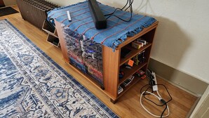 Een houten tv-meubel met een blauw en oranje vloerkleed, een afstandsbediening en diverse gezelschapsspellen.