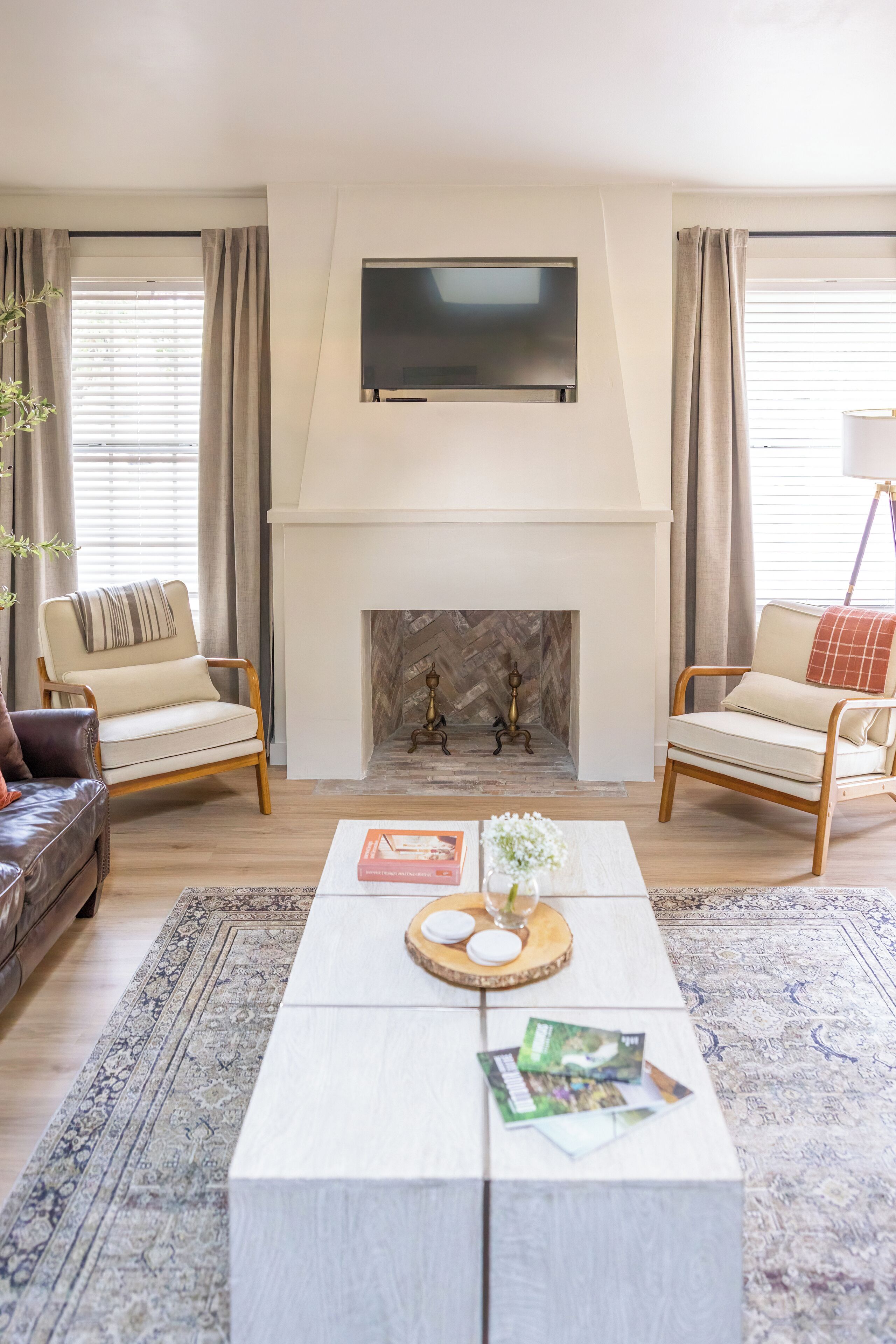 Una sala de estar con chimenea, dos sillones, una mesa de centro y un televisor sobre la chimenea.
