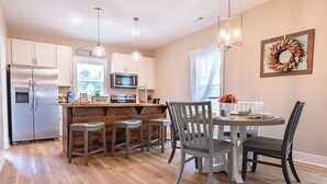 A modern kitchen with stainless steel appliances, a wooden island with bar stools, and a dining area with a round table and chairs. - Pet Friendly! Cozy Beach Cottage Minutes to Downtown and ILM-Fenced Backyard! (Wilmington)