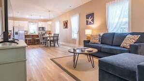 A modern living room with a sofa, coffee table, and a TV. There is a kitchen area in the background with a dining table and chairs. - Pet Friendly! Cozy Beach Cottage Minutes to Downtown and ILM-Fenced Backyard! (Wilmington)