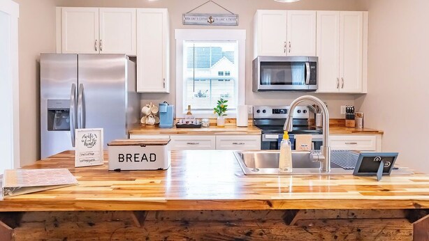 A modern kitchen with white cabinets, stainless steel appliances, a wooden island, and pendant lights. - Pet Friendly! Cozy Beach Cottage Minutes to Downtown and ILM-Fenced Backyard! (Wilmington)