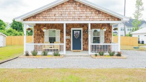 A two-story building with a wooden facade, a front porch with white railings, and a dark blue door. - Pet Friendly! Cozy Beach Cottage Minutes to Downtown and ILM-Fenced Backyard! (Wilmington)