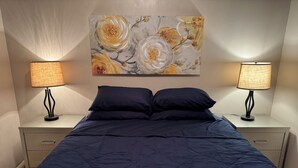 Une chambre à coucher avec un grand lit, deux tables de chevet avec des lampes et un tableau floral accroché au mur.