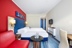 Een hotelkamer met een bed, een rode fauteuil, een klein tafeltje met glazen, een televisie en een schilderij aan de muur.
